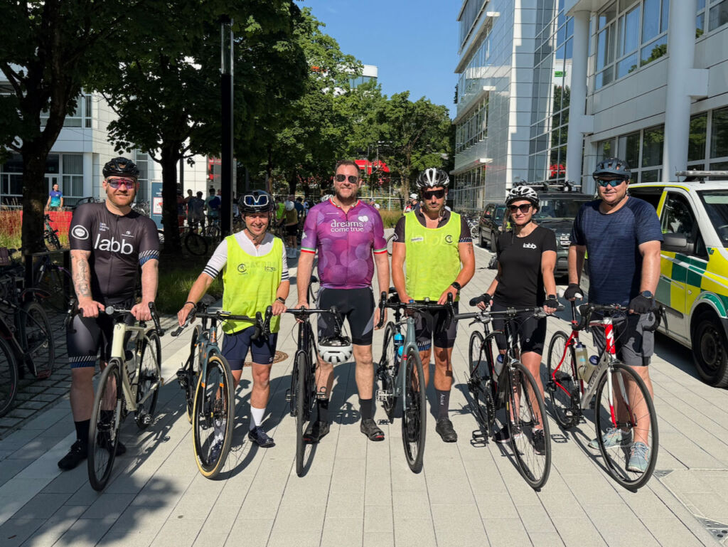 a team of cyclists lining tip against their bikes before taking part in a long distance cycling challenge. All are wearing lycra and standing next to their bikes